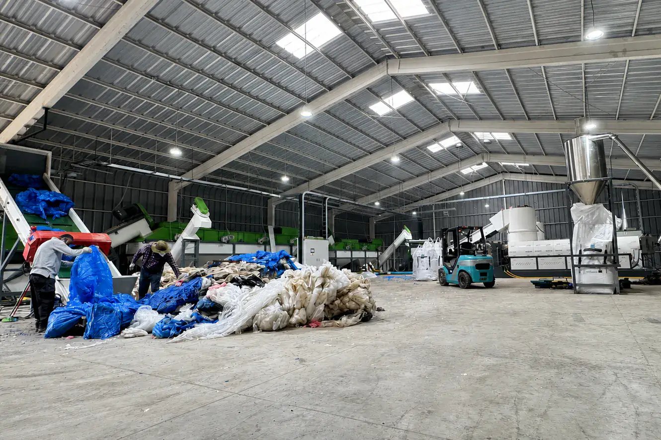 Film washing and pelletizing plant with workers sorting bales of used film next to the washing line