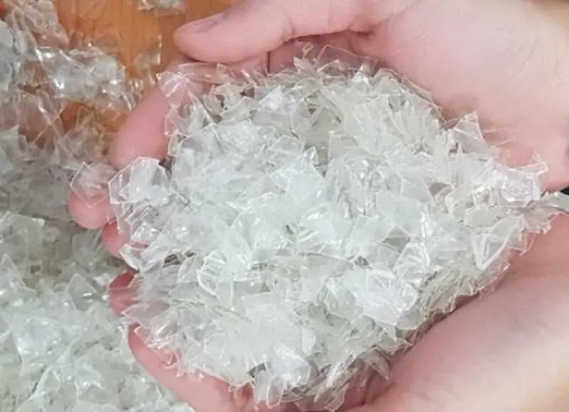 A handful of clean, clear washed PET flakes held over a pile of flakes